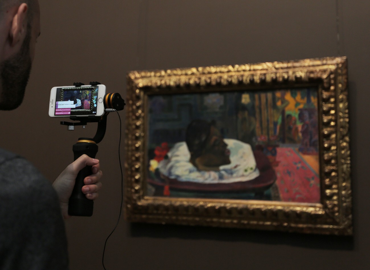 Andrew Westover holds an iphone facing a Gauguin painting.