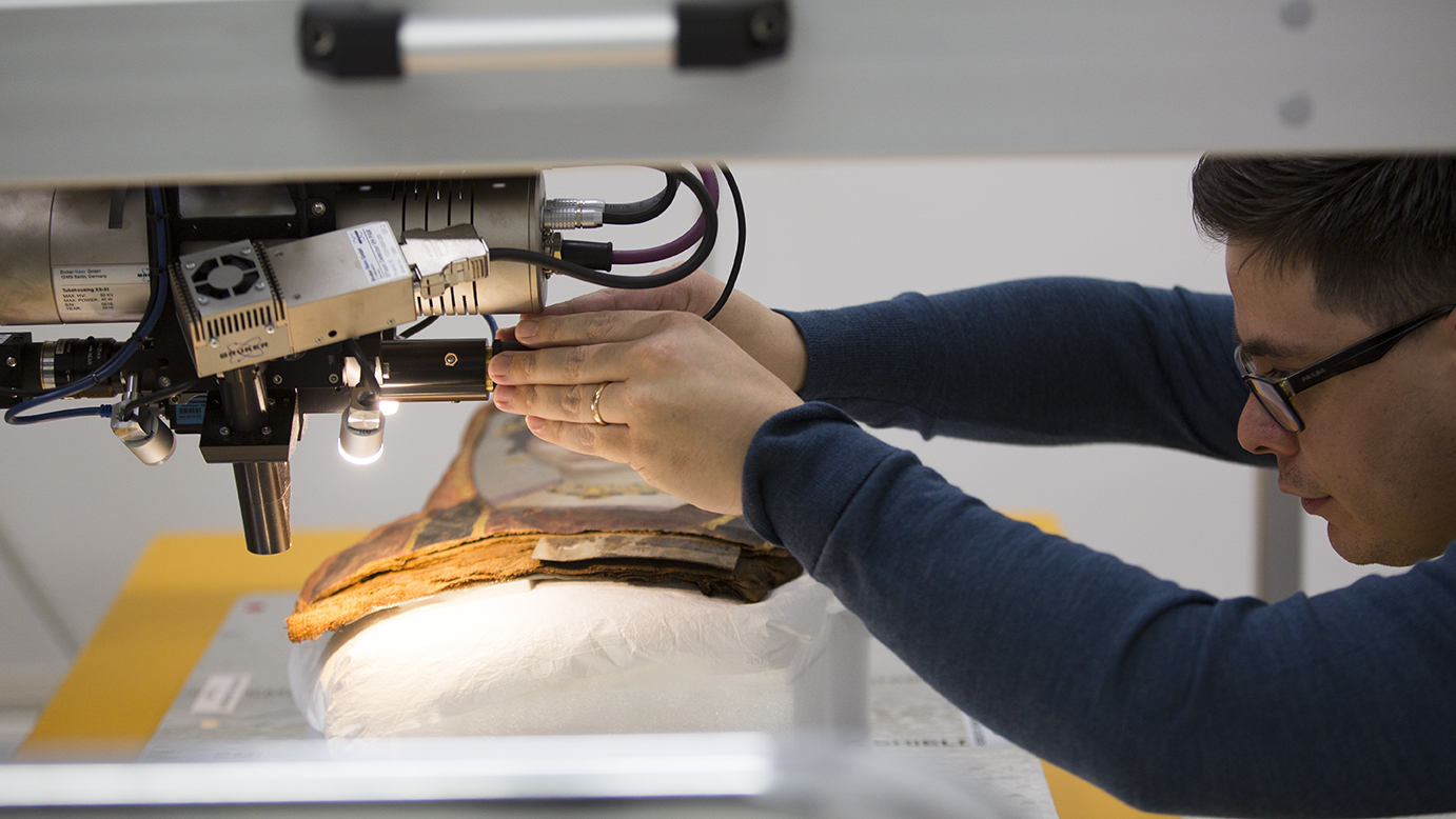 Close-up side view of a young man positioning analytical equipment to image an ancient Romano-Egyptian portrait on wood