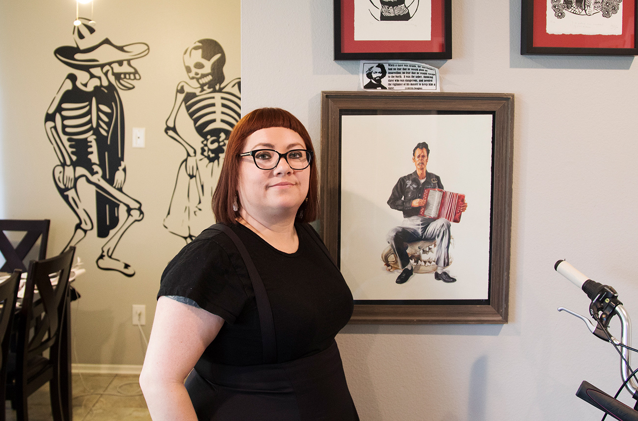 Isabel Quintero standing in her home with an illustration by Zeke Pena. The two collaborated on Photographic: The Life of Graciela Iturbide.