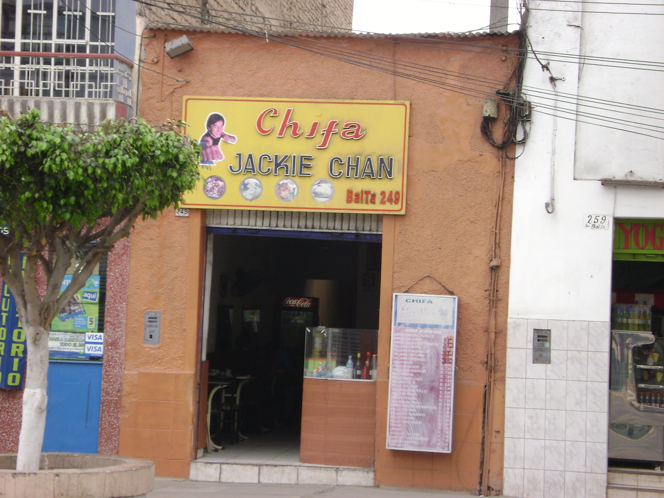 Exterior of a modest restaurant with stucco walls and a bright yellow and red sign reading "chifa"