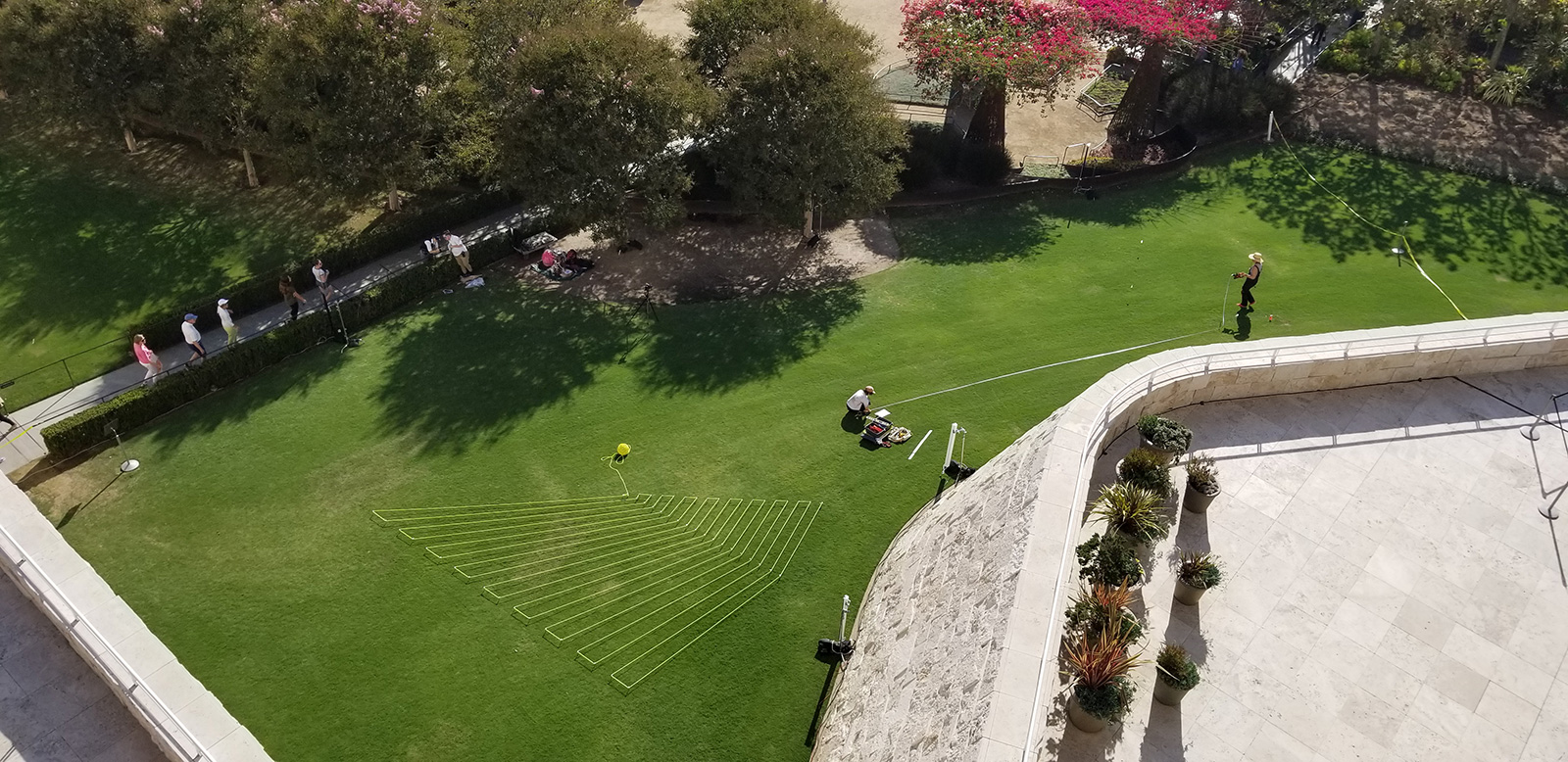Overhead view of two women working with a long, thick spool of brightly painted rope on a large green lawn