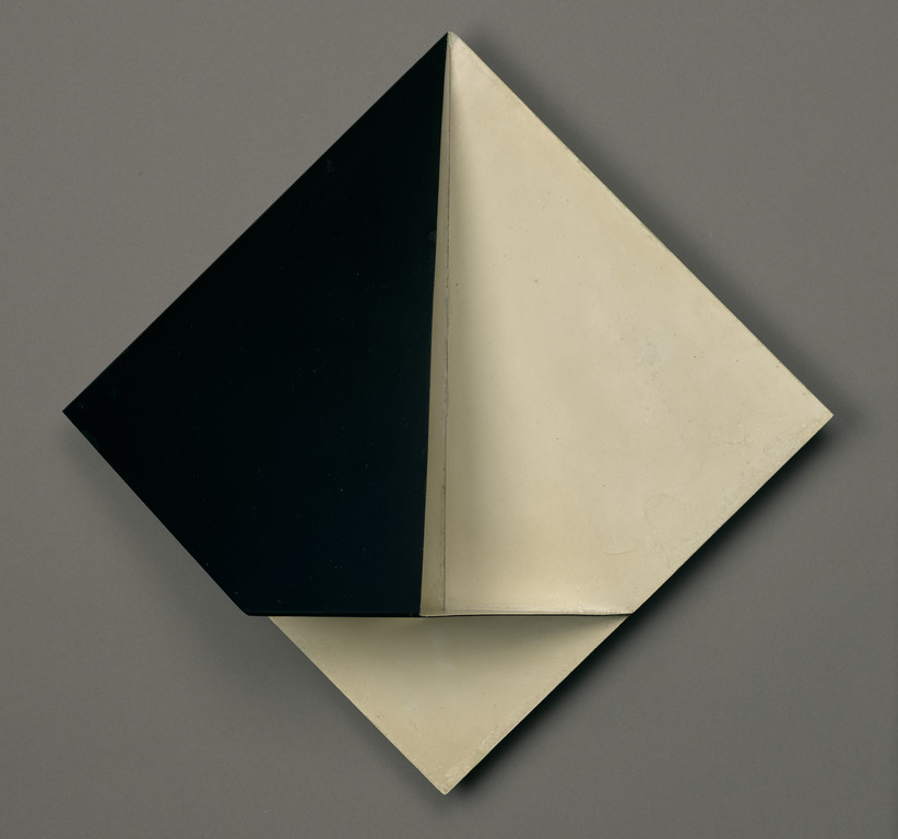 Front view of a black and white, geometric, sculptural painting that juts out in the center from the wall