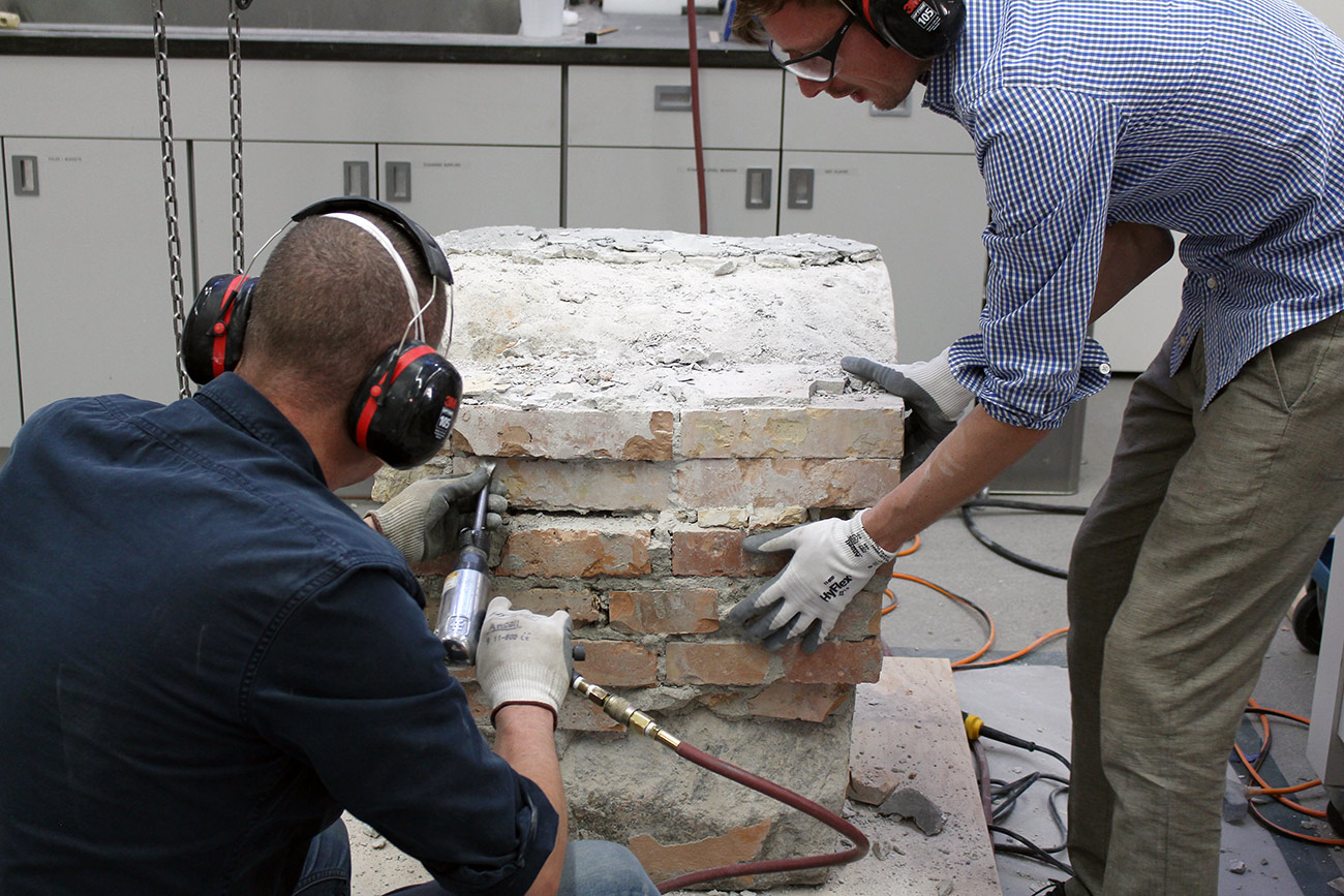 Two conservators bend over a stone and brick structure