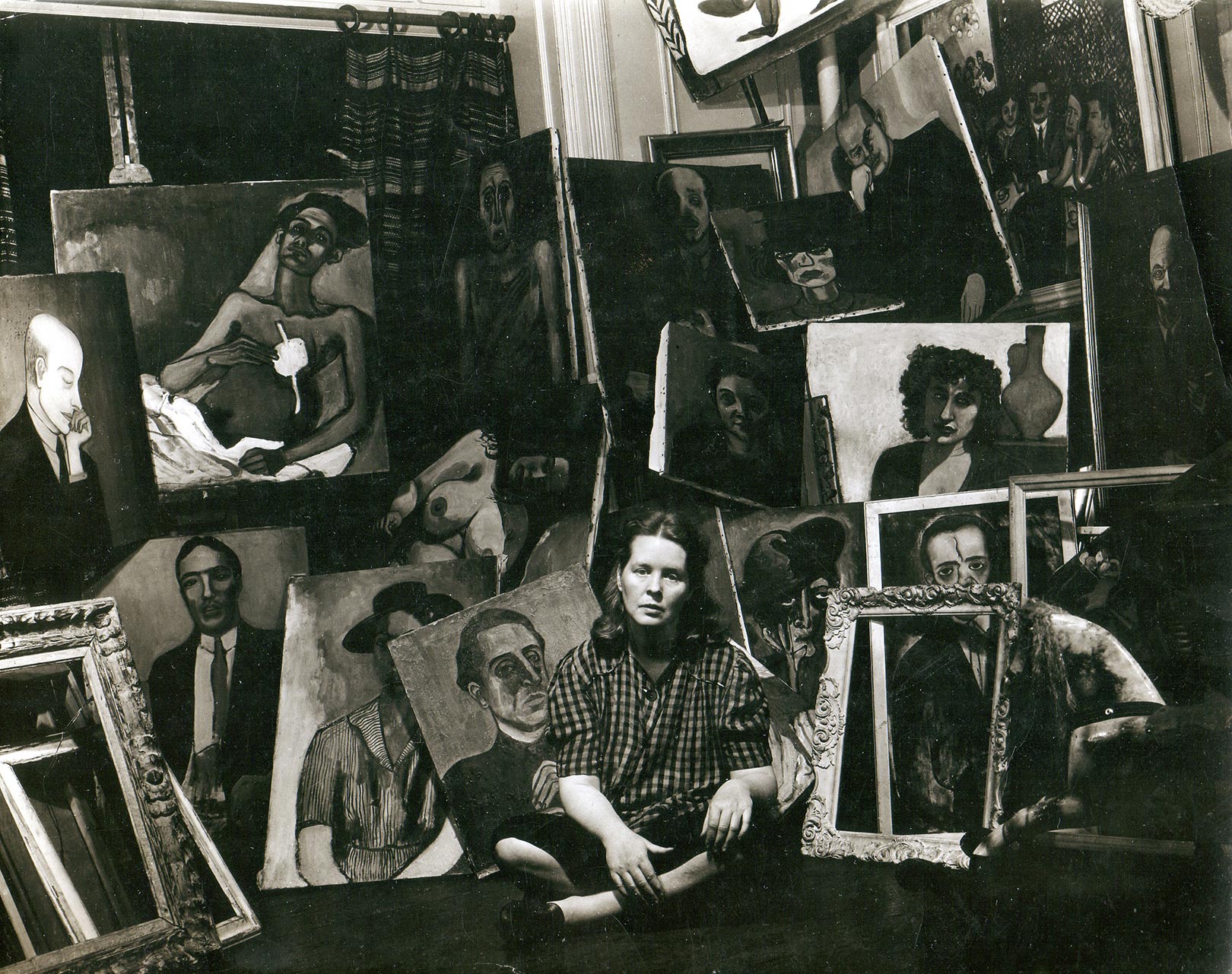 Alice sits cross-legged on the floor, surrounded by many paintings.