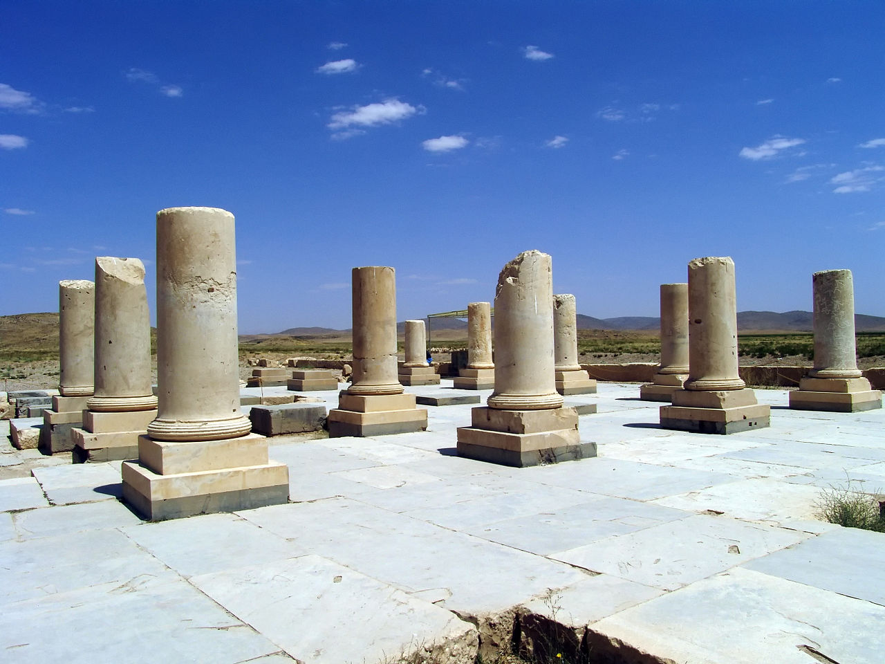 Columns stand in ruins against a bright blue sky in Iran