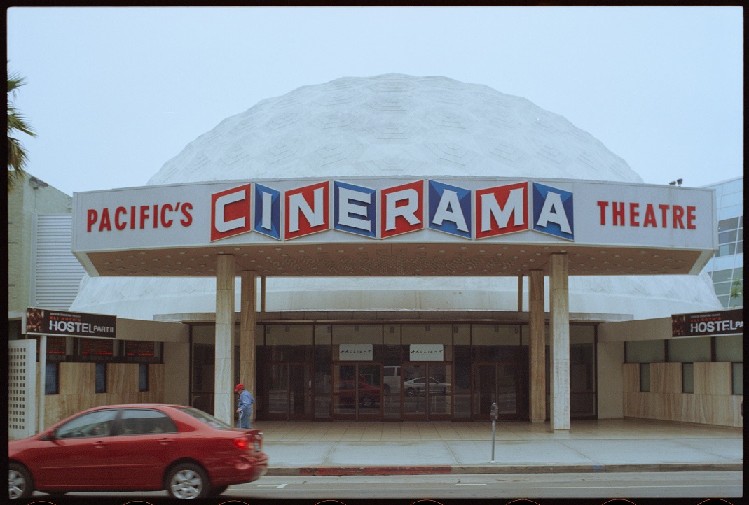 Color photograph of the Cinerama movie theater with a red car parked in front