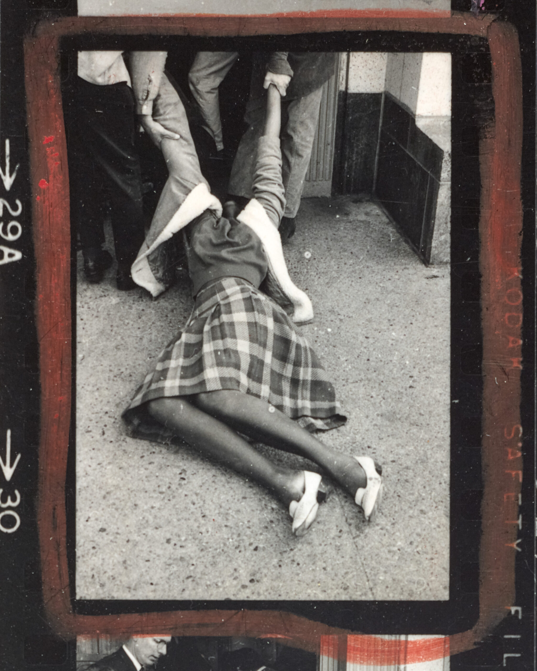 A black and white photographic image, outlined in red wax pencil, shows a Black woman, head back, being dragged by two white figures out of frame. Only the white hands are visible.