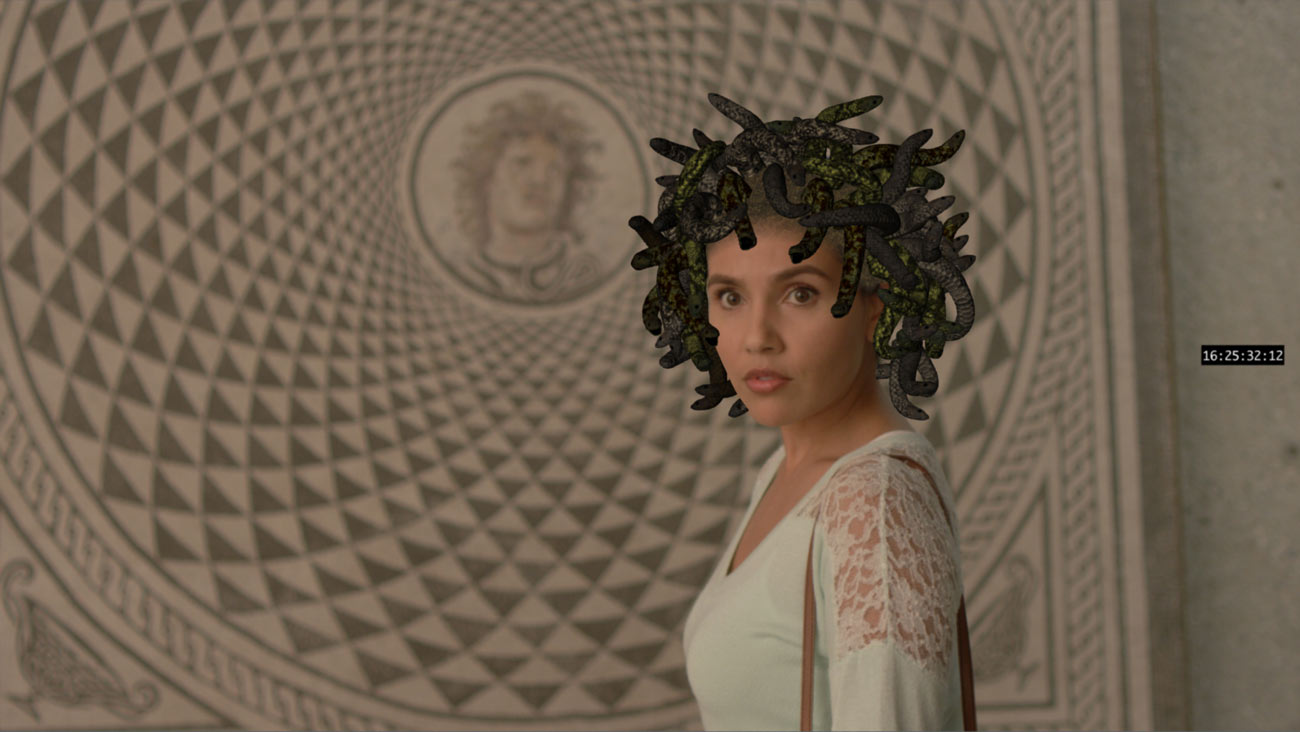 A woman stands in front of a mosaic of Medusa with a tangle of computer generated snakes on her head.