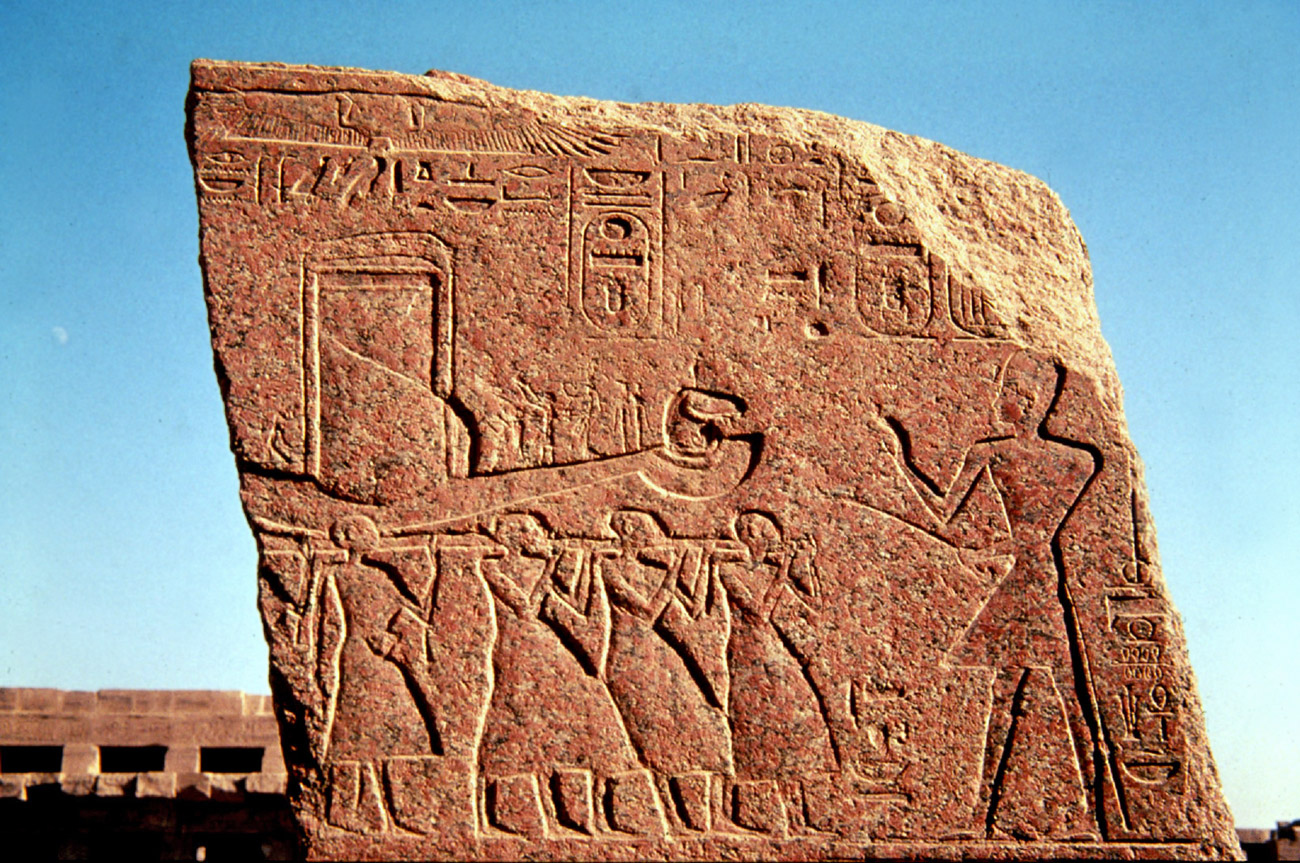 A relief carved in stone showing Egyptian style figures          carrying a boat with hieroglyphics above.