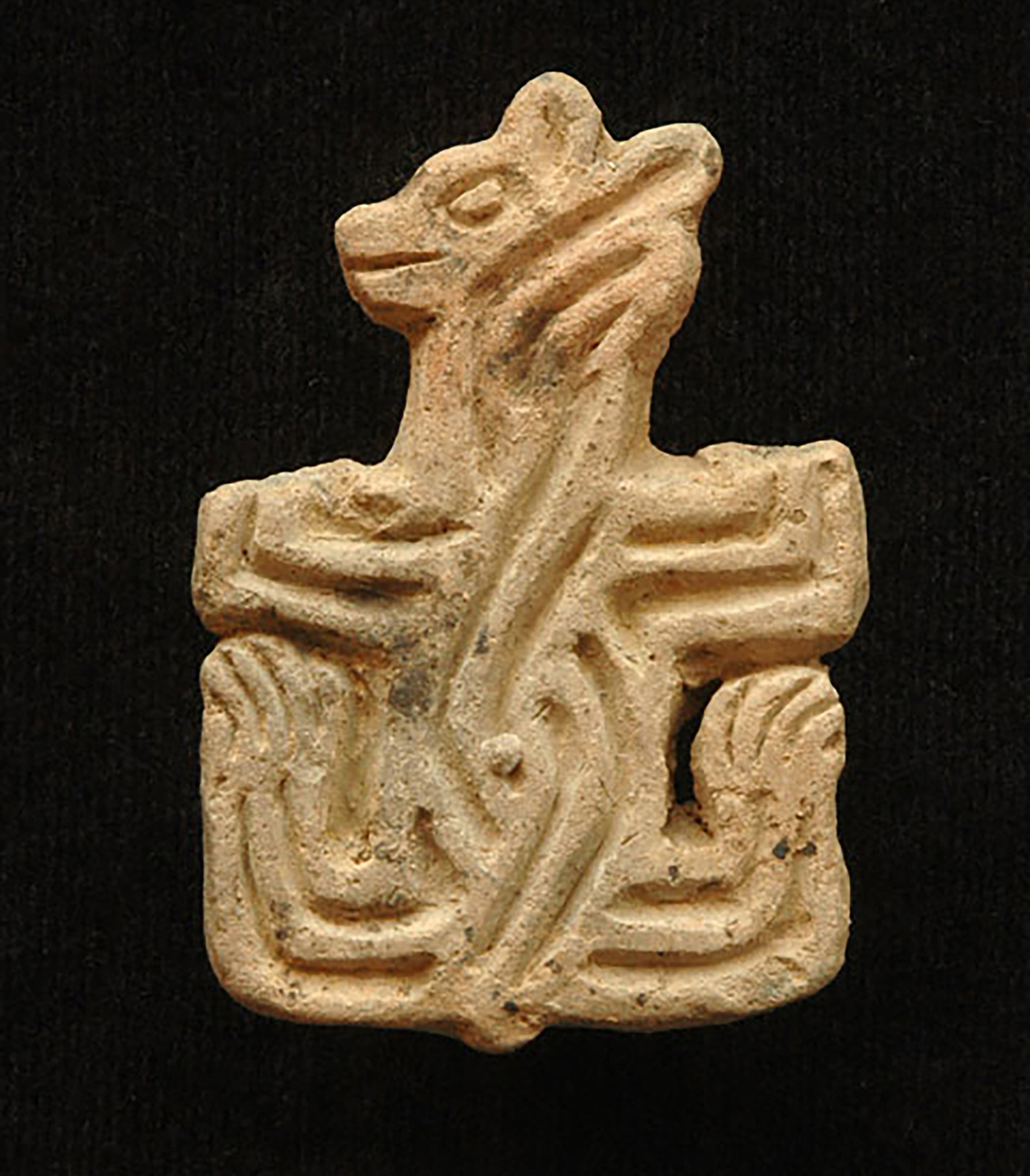 Ancient stone carving of a mammal with large paws and small ears, ornamented with sinuous lines
