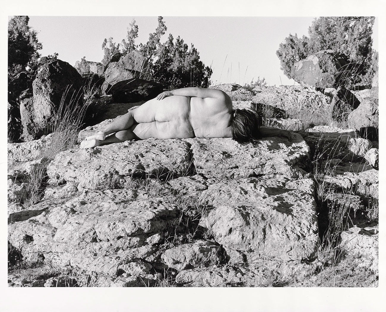 Aguilar, nude, lies on her side on a large rock with her back to the camera.