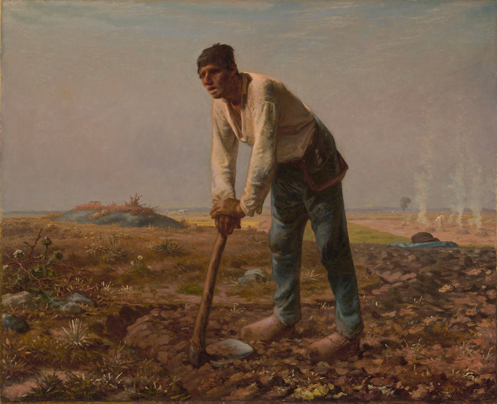 A man in a white shirt and jeans leans on a hoe in a field