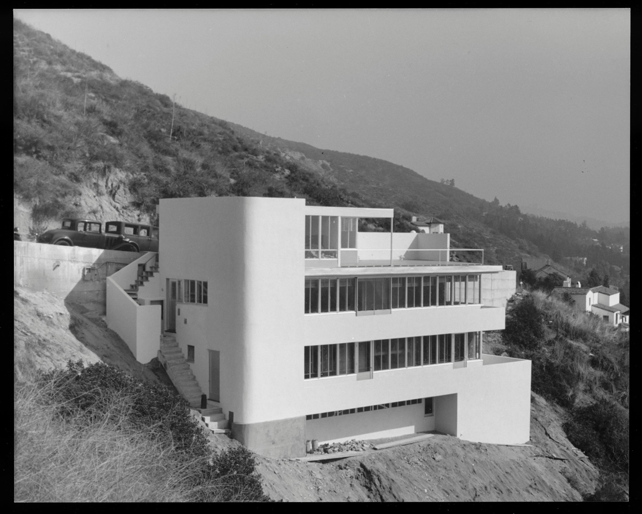 Black and white photo of four story home built into side of cliff overlooking a canyon