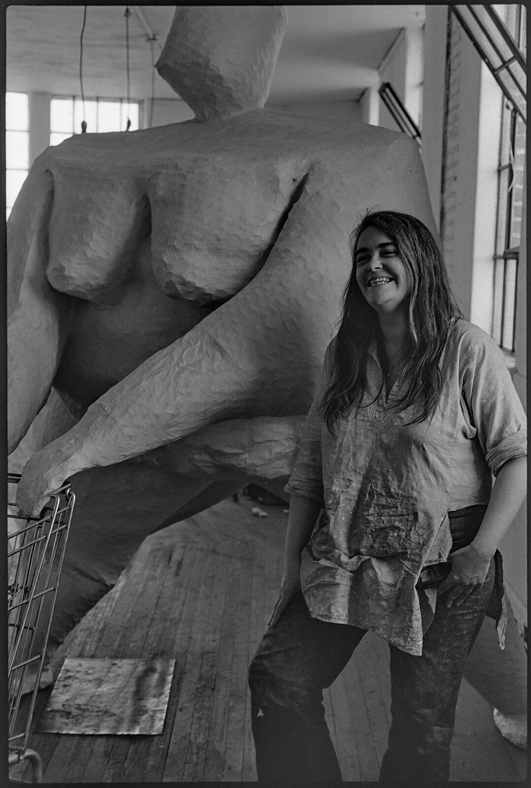 Millett stands with large sculpture of nude woman pushing a shopping cart