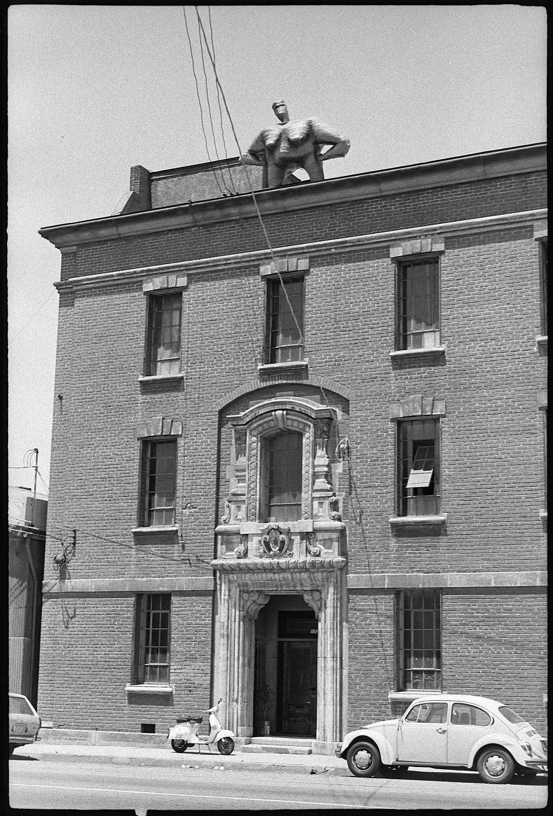 Three story brick building with sculpture of nude female figure on the roof