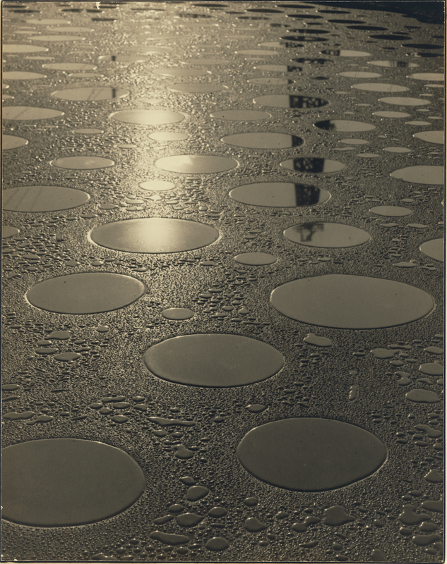 <em>Reflections on the Oil Ditch</em>, about 1925, Shigemi Uyeda. Gelatin silver print, 13 3/16 × 10 7/16 in. The J. Paul Getty Museum, 2019.58.1. © Family of Shigemi Uyeda Black and white image of reflective circles of different sizes on the ground