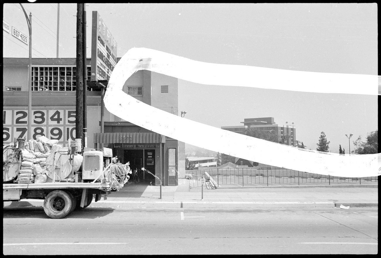 Back of truck driving by building with The Trip written on the marquee; the image has a white strip painted across it