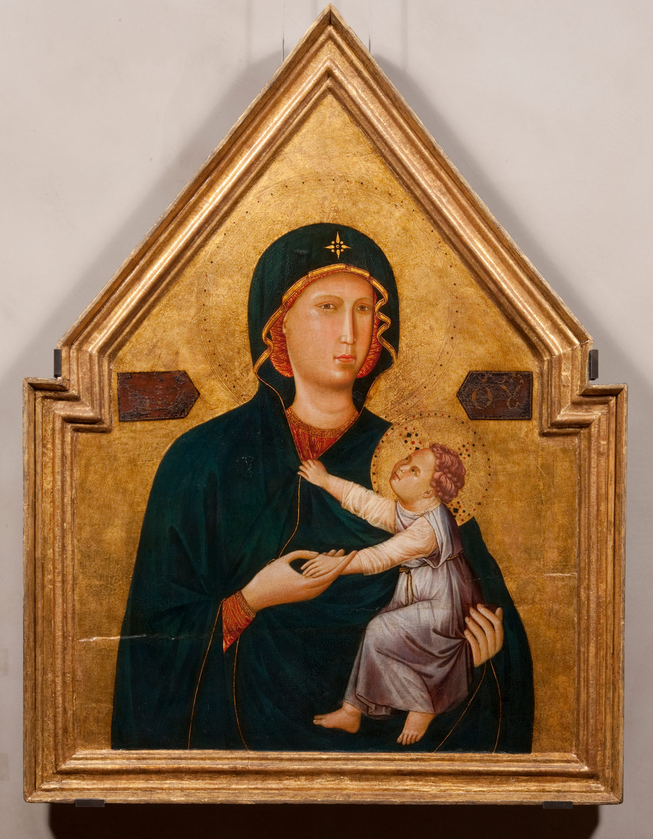 Triangle shaped painting of the Madonna holding the Christ Child, surrounded by a gold carved border