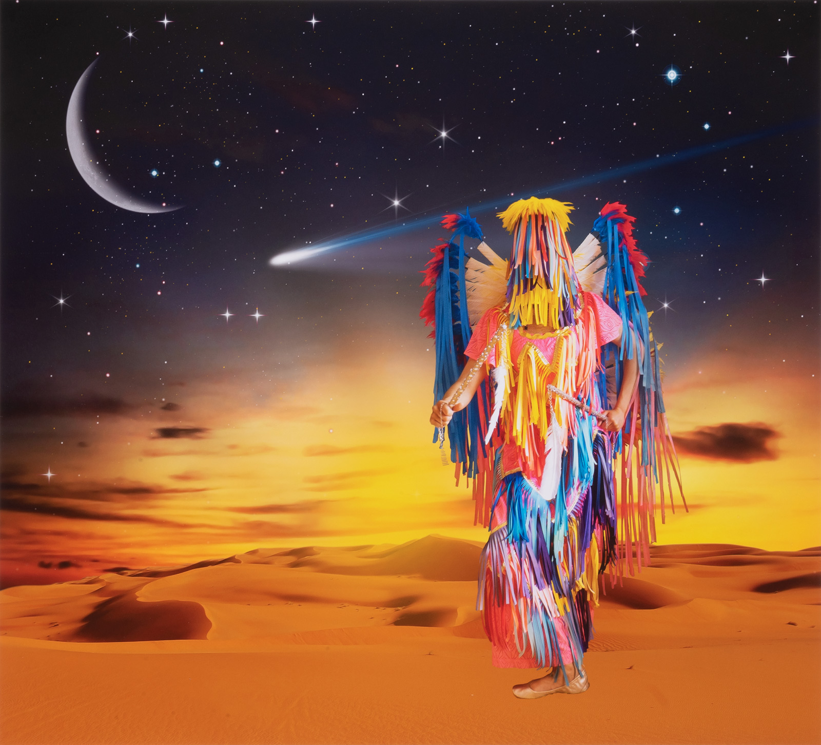 person in red, yellow and blue feathered costume dances in the orange desert