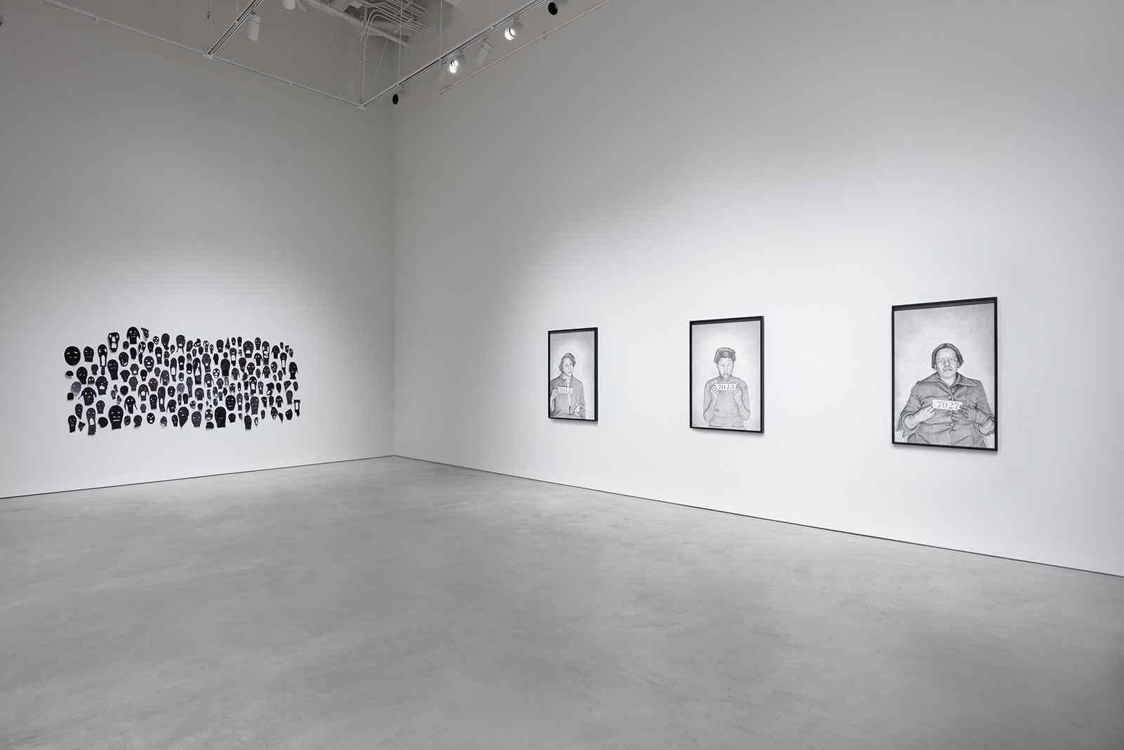 Gallery with black masks on the left wall, three framed pencil drawings on the right wall