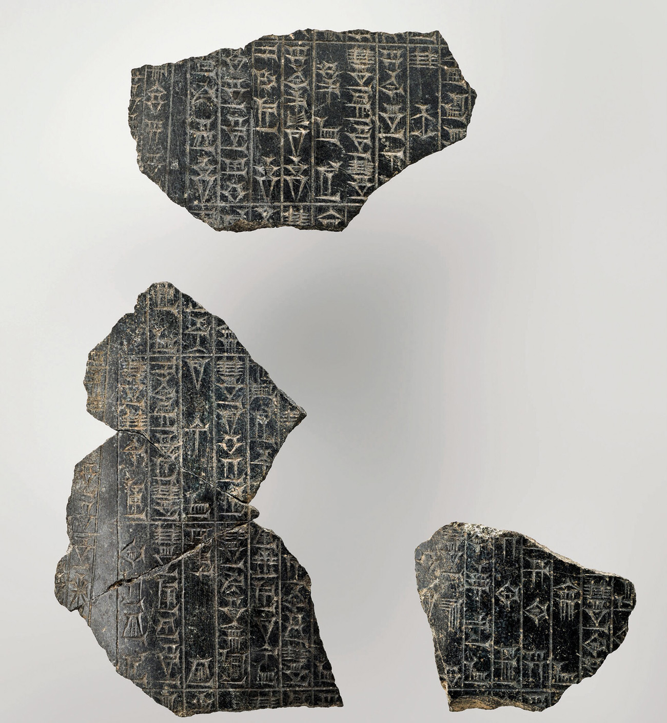 Three irregularly shaped pieces of smooth black rock with rows of shapes and characters etched into them