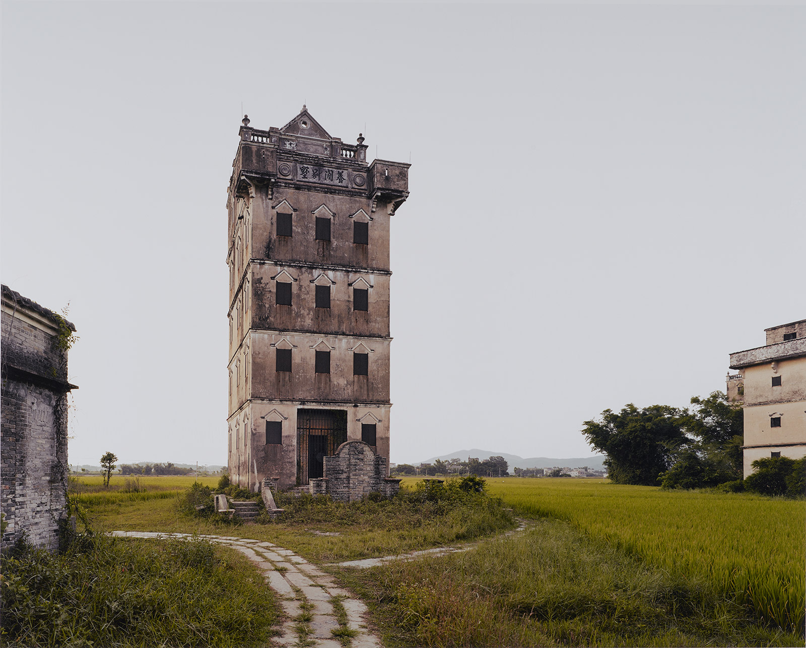 A tall, weathered building stands alone in a field on an overcast day