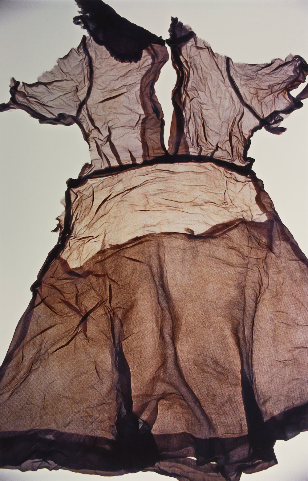 A wrinkled, beige dress is spread flat and backlit.