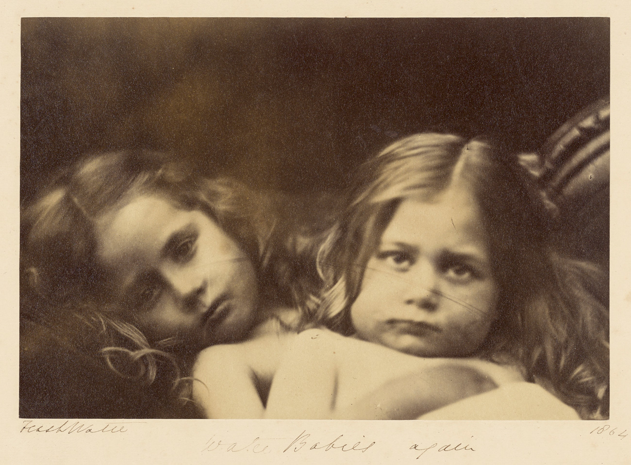 Two young children lying down, looking at the camera, with one child resting their head on the other child’s chest