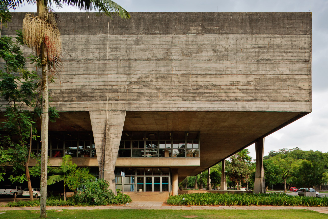 Large concrete building with two floors covered in windows, topped with a thick concrete roof supported by columns