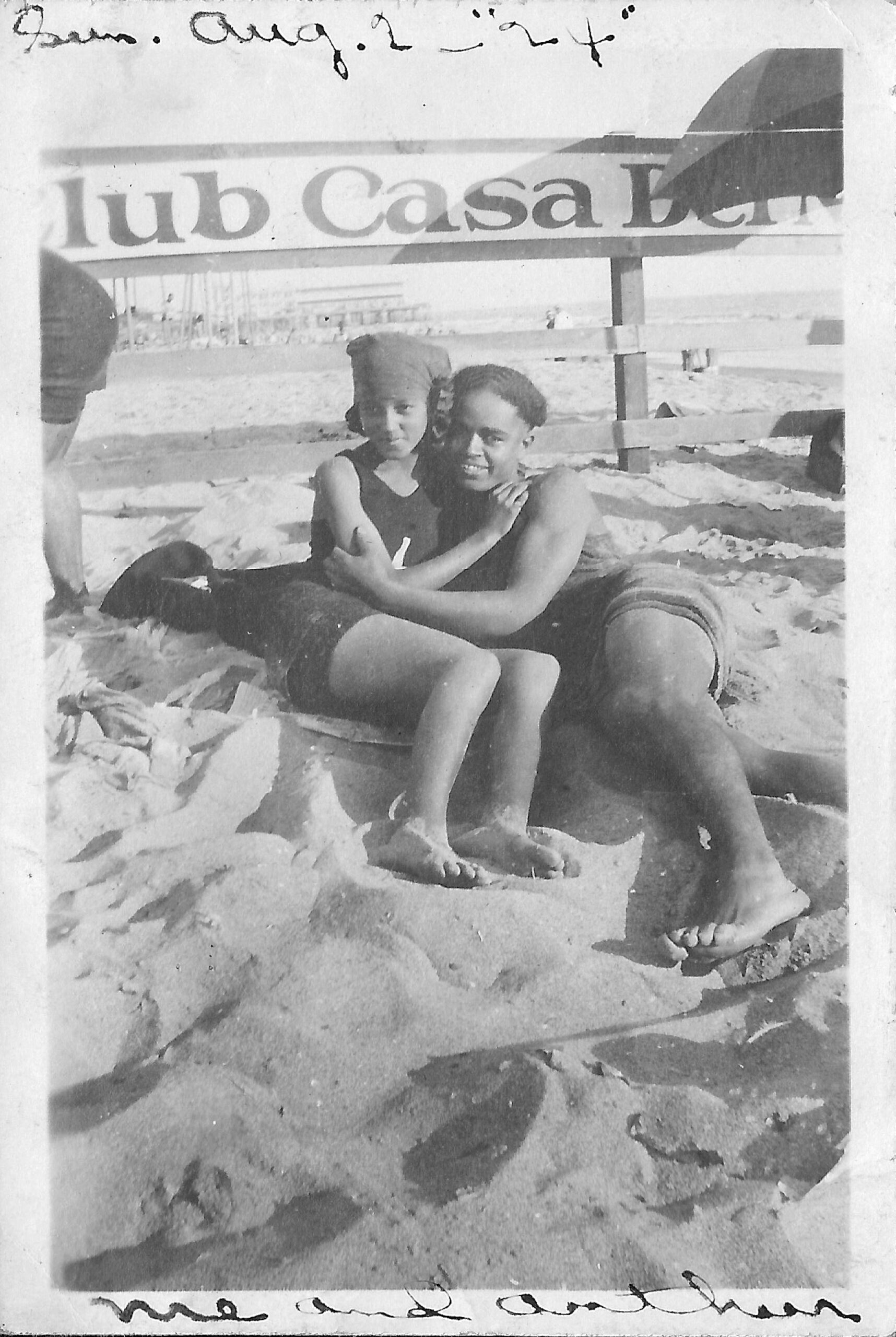 Newlyweds Verna Deckard and Arthur Lewis, posing in front of the Casa del Mar Club fence sign at the Santa Monica beach, August 2, 1924. Photo: From the Verna Deckard L. Williams Collection of Arthur and Elizabeth Lewis Photo of African American couple lounging on the beach together, in front of a sign that reads Casa del Mar Club, from August 2, 1924