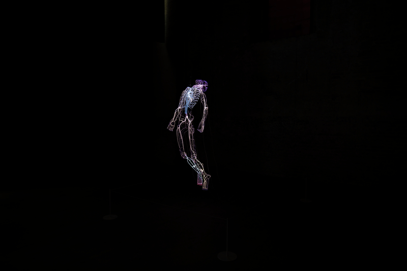 Robert, 2018, Tavares Strachan. Neon, Pyrex, transformers, medium-density fiberboard box, dimensions variable. Collection of the artist Black background with a neon sculpture in the shape of the blood vessels of a human body. The human form has their head back and appears to be floating or ascending.