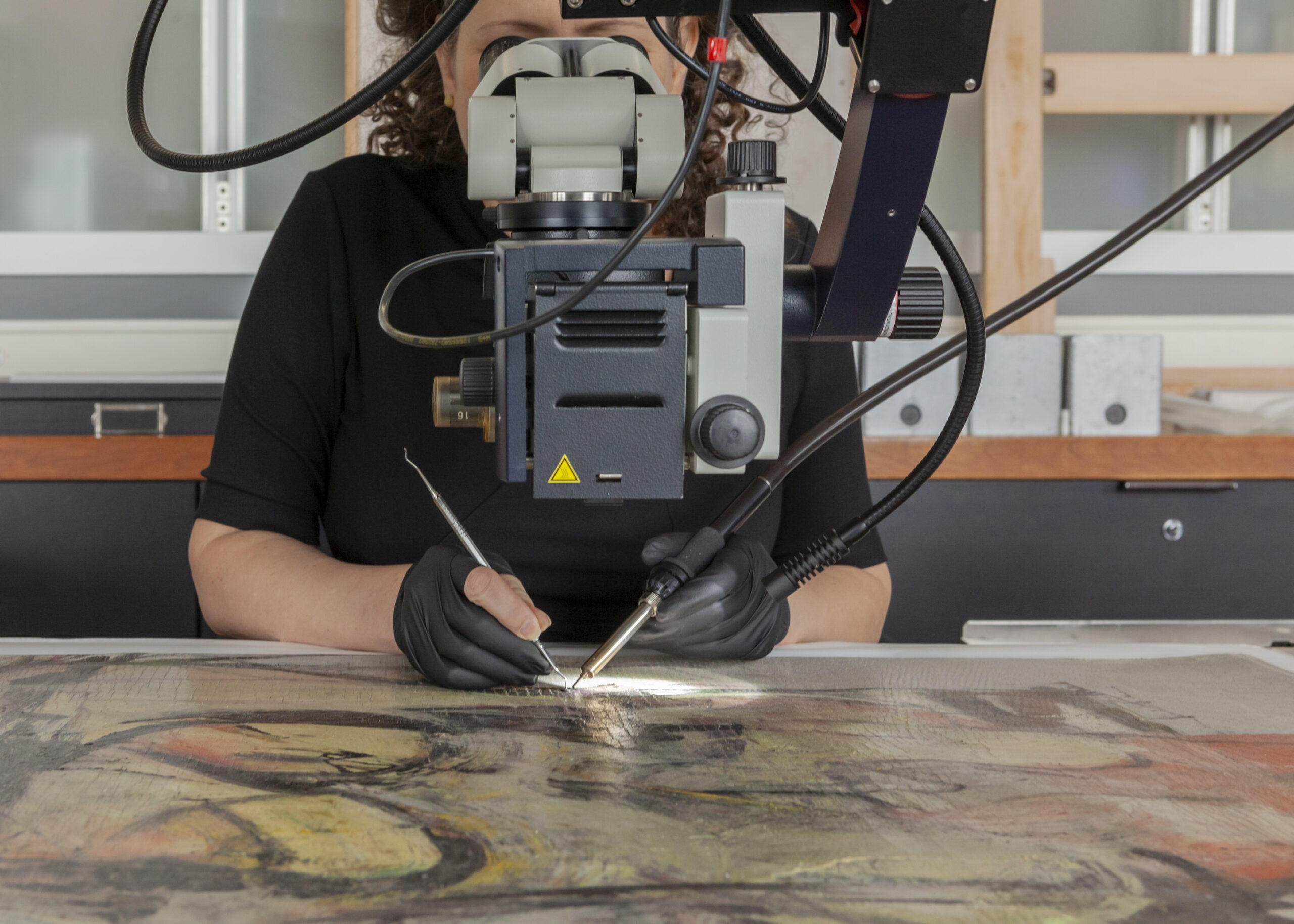 Woman-Ochre, 1954–1955, Willem de Kooning. Oil on canvas, 40 × 30 in. © 2022 The Willem de Kooning Foundation / Artists Rights Society (ARS), New York de Kooning's Woman-Ochre is on a table while a person looks at it through a machine. The person works on the canvas using dental tools.